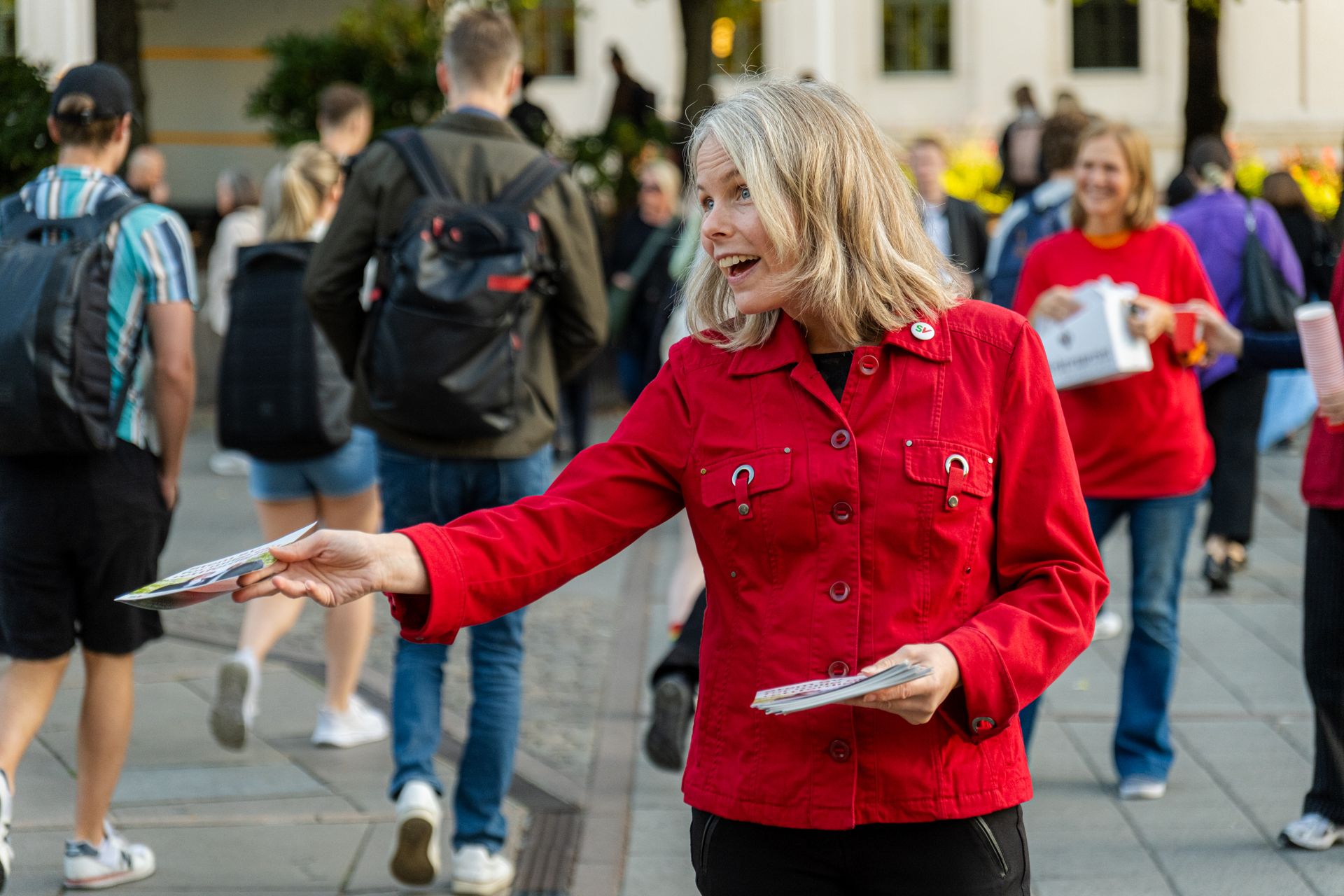 Kirsti Bergstø i rød jakke deler ut løpesedler til folkemengde